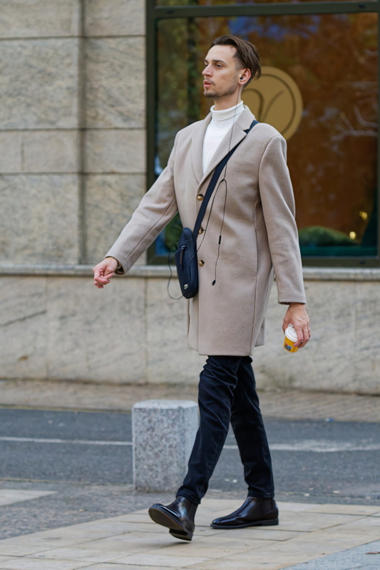 19 - A man wearing a smart-casual autumn outfit featuring a beigetan overcoat, a white turtleneck sweater, dark trousers, and leather boots